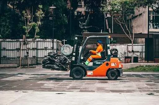 Forklift operator maneuvering a forklift with attachments, transporting materials in a warehouse setting, highlighting efficiency and safety in material handling.