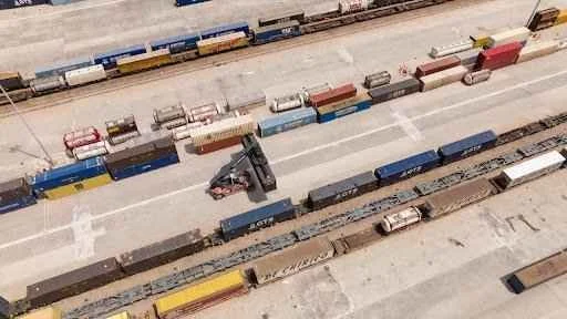 Aerial view of a forklift navigating between shipping containers in a logistics yard, illustrating efficient loading and unloading operations relevant to forklift container ramp maintenance.
