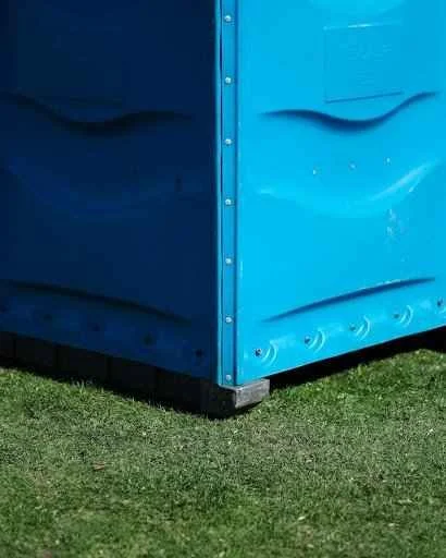 Blue portable toilet on grass, highlighting the importance of maintenance and hygiene for outdoor events and construction sites.
