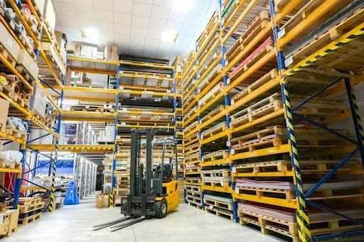 Forklift in a warehouse surrounded by stacked pallets, illustrating efficient material handling and storage solutions relevant to forklift attachments suppliers.