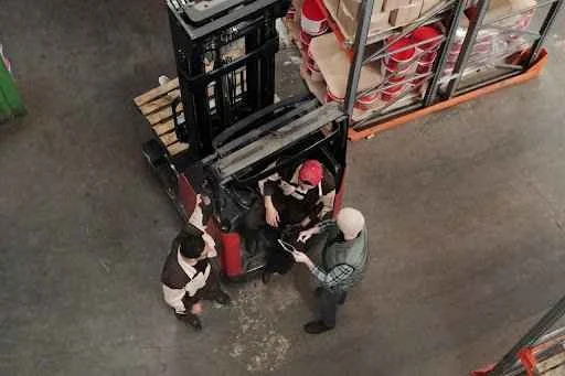 Workers discussing forklift operations in a warehouse setting, showcasing the importance of forklifts in logistics and material handling.