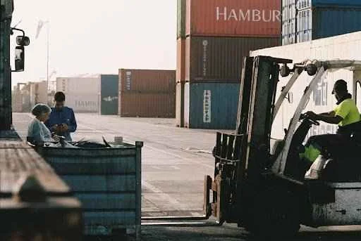Forklift operator maneuvering near shipping containers in a logistics yard, illustrating efficient loading operations with portable container ramps.