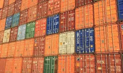 Colorful stack of shipping containers in various sizes and brands, showcasing logistics and supply chain operations.