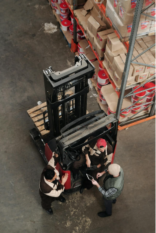 Warehouse workers discussing forklift operations, surrounded by storage boxes and equipment, emphasizing the importance of forklift accessories for safety and efficiency.