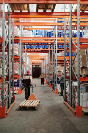 Warehouse interior with pallet jacks being used for material handling, showcasing organized shelving and various products, emphasizing efficiency in logistics and storage.