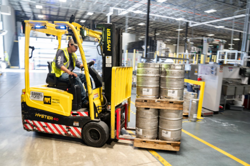 Forklift operator maneuvering a Hyster forklift with stacked kegs in a warehouse setting, illustrating efficient material handling in industrial operations.