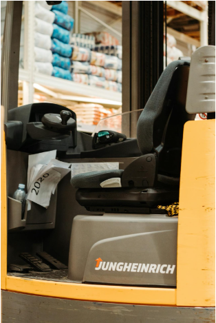 Forklift operator's seat and control panel featuring Jungheinrich branding, set against a backdrop of warehouse materials.