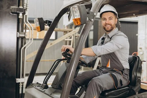 Man operating a forklift in a warehouse setting, wearing safety gear, illustrating forklift operation and safety in material handling.