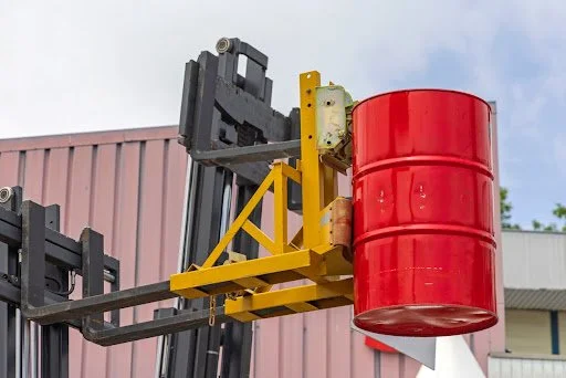 Forklift equipped with a yellow drum handler lifting a red barrel, emphasizing essential accessories for safety and efficiency in warehouse operations.