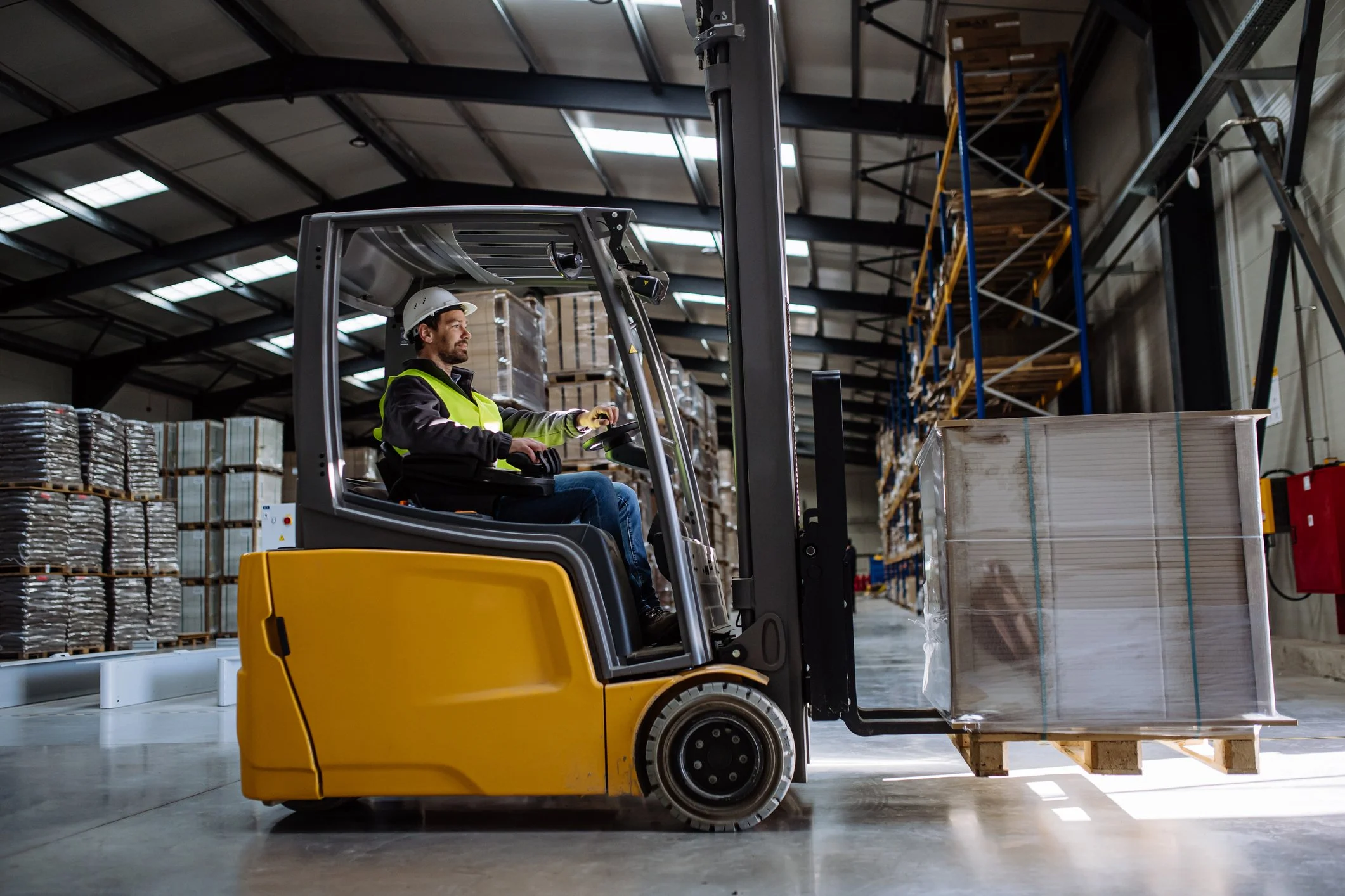 Forklift operator maneuvering a yellow forklift in a warehouse, surrounded by stacked pallets, illustrating equipment use for material handling in Australia.