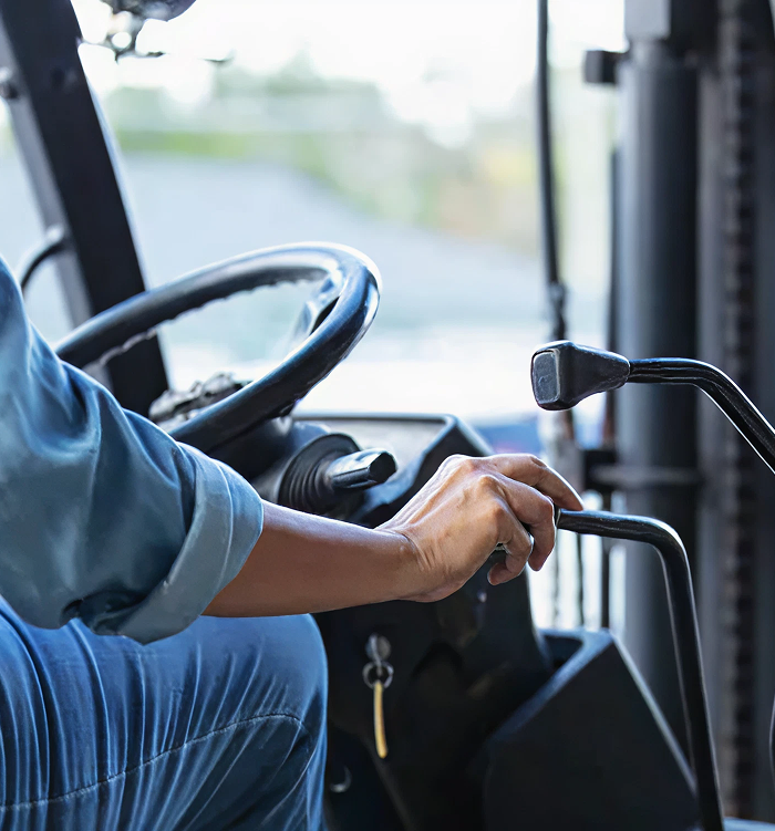 Person operating a forklift, focusing on the steering wheel and control lever, illustrating the importance of quality transmission parts for industrial equipment.