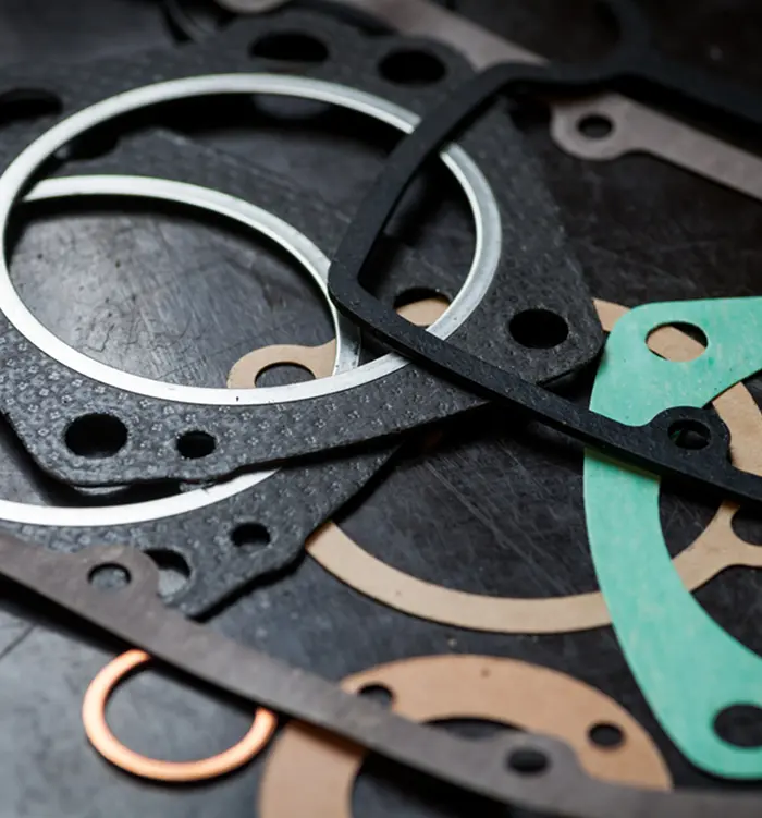 Assorted engine gaskets and sealing components on a dark surface, showcasing various shapes and materials for industrial equipment maintenance and repairs.