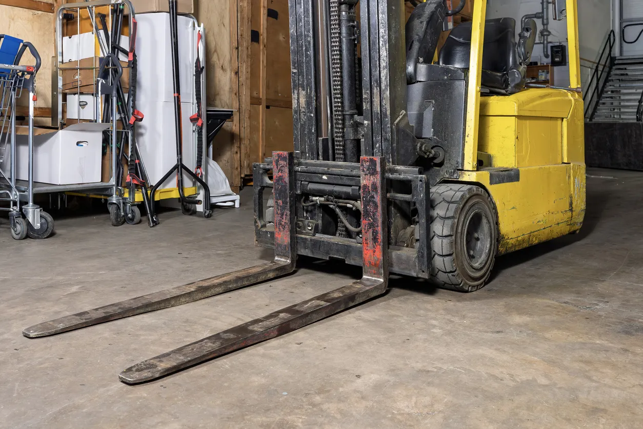 Forklift with worn tynes in a warehouse setting, highlighting essential maintenance for safety and operational efficiency.