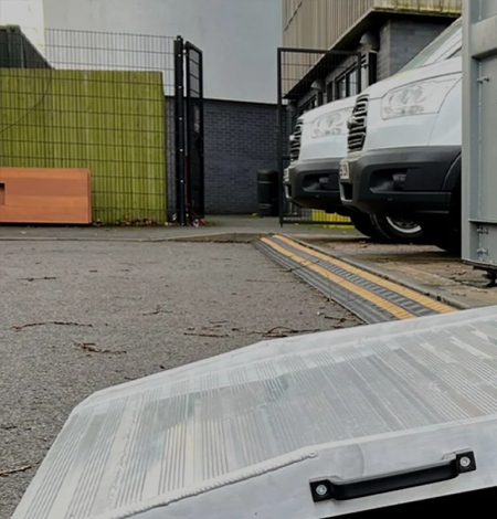 Container ramp positioned on a loading area with parked vans in the background, illustrating warehouse equipment solutions for efficient logistics operations.